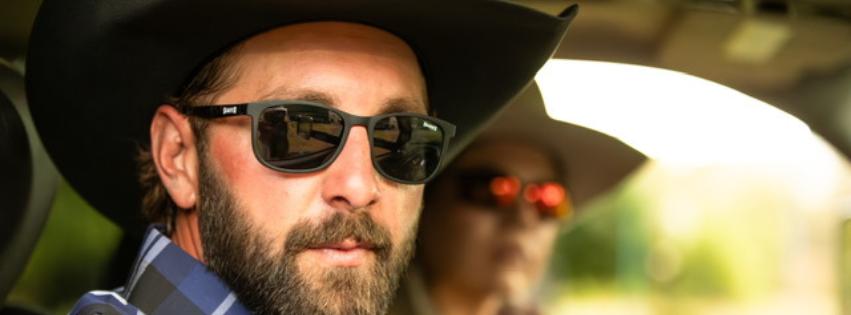 Man in a check shirt, with a Western hat on wearing Branded Sunglasses and swinging a rope